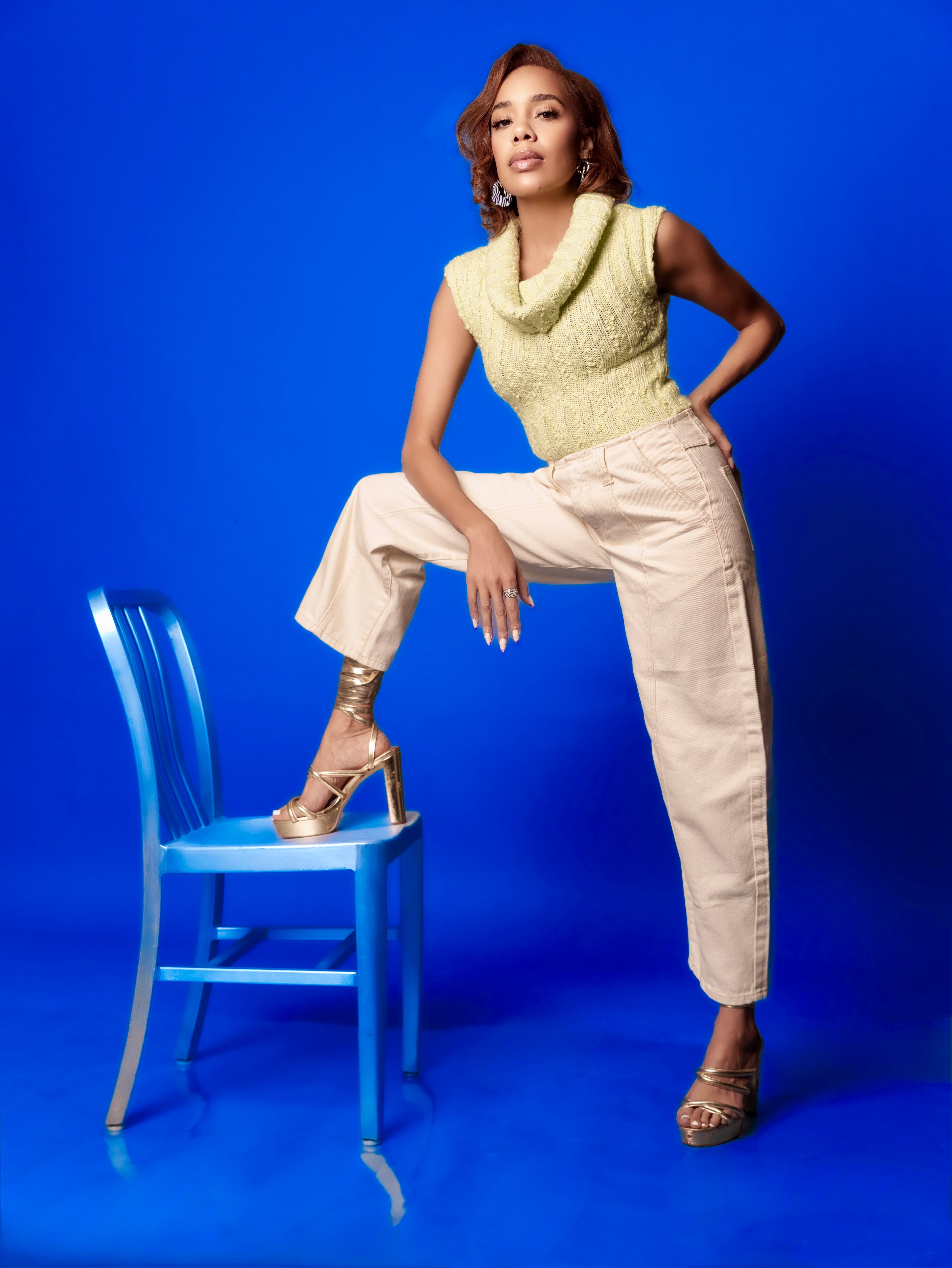 Woman in a green sleeveless top and beige pants posing on a blue chair against a blue background | B. Marie Accessories, Shannon Johnson, DMV
