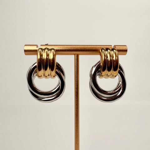 Pair of gold and silver hoop earrings on a stand against a light background