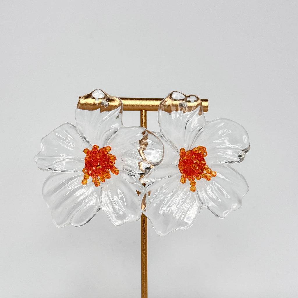 Flower-shaped earrings with orange centers on a gray background