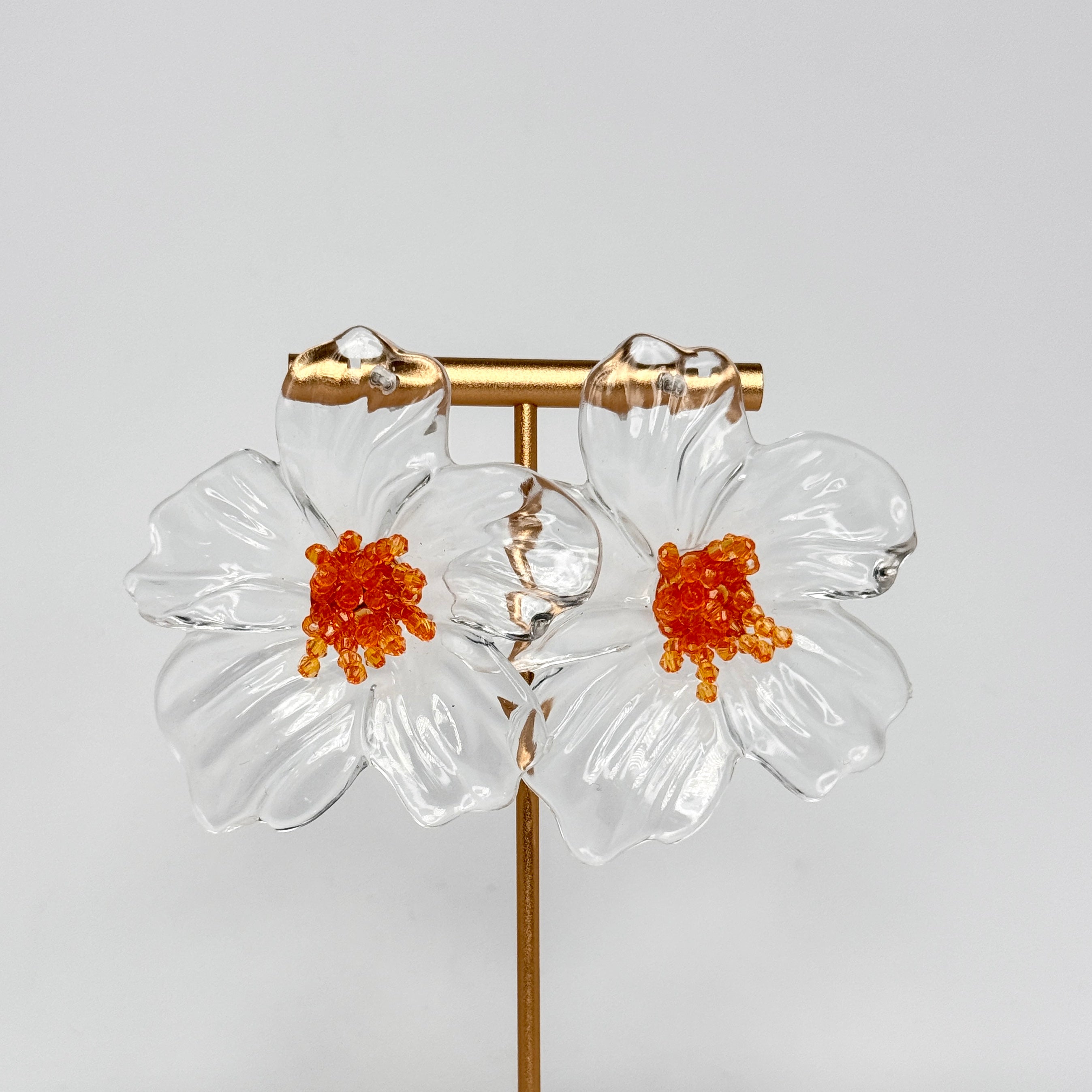 Flower-shaped earrings with orange centers on a gray background