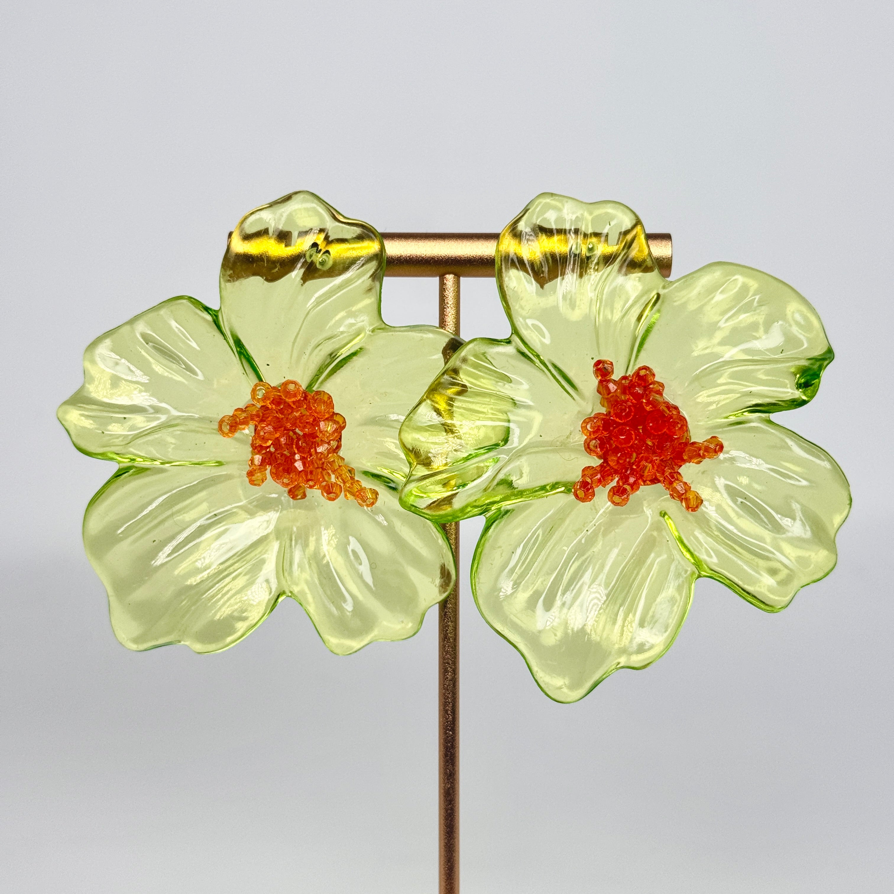 Pair of green floral earrings with orange centers on a light gray background
