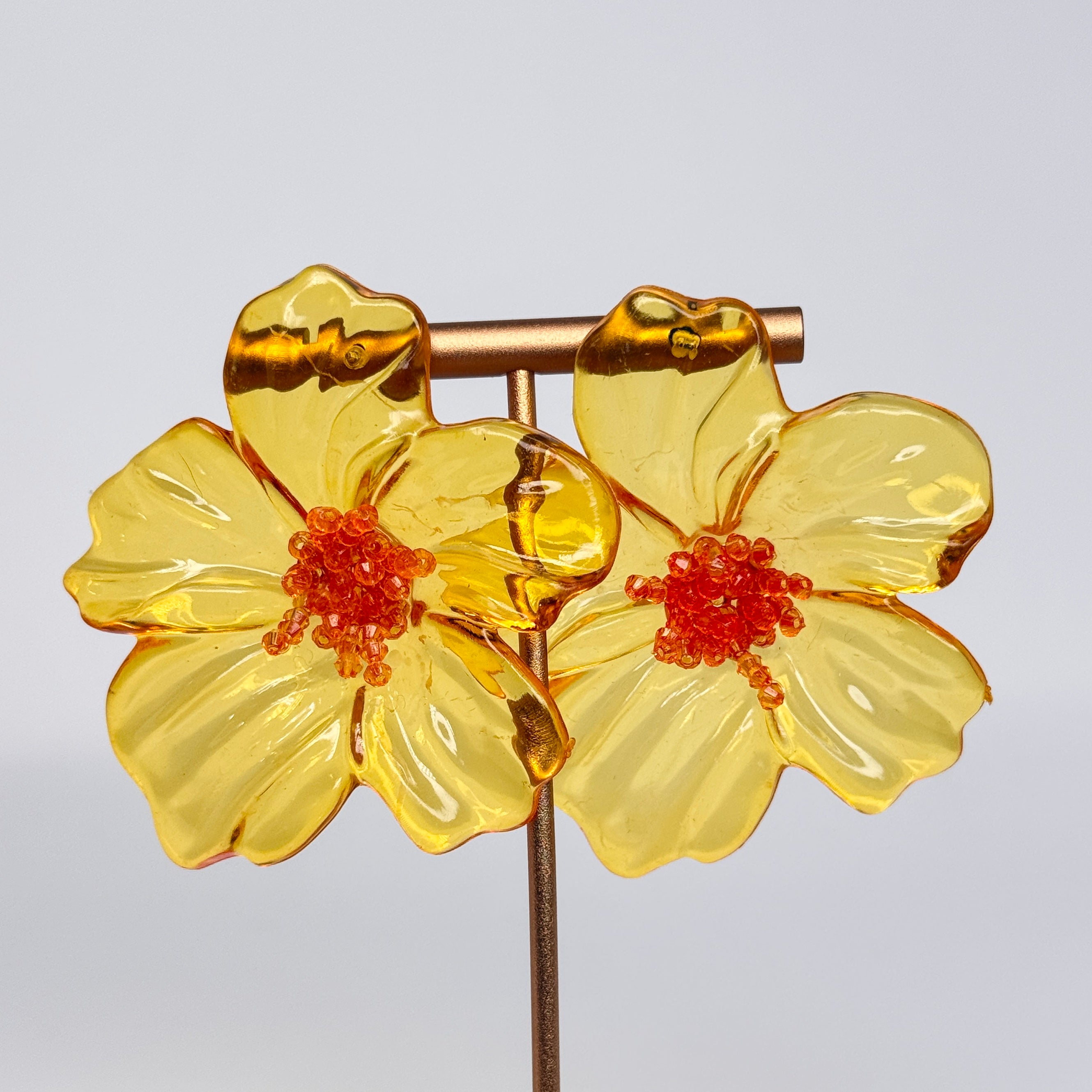 Pair of yellow floral earrings with orange centers on a light gray 